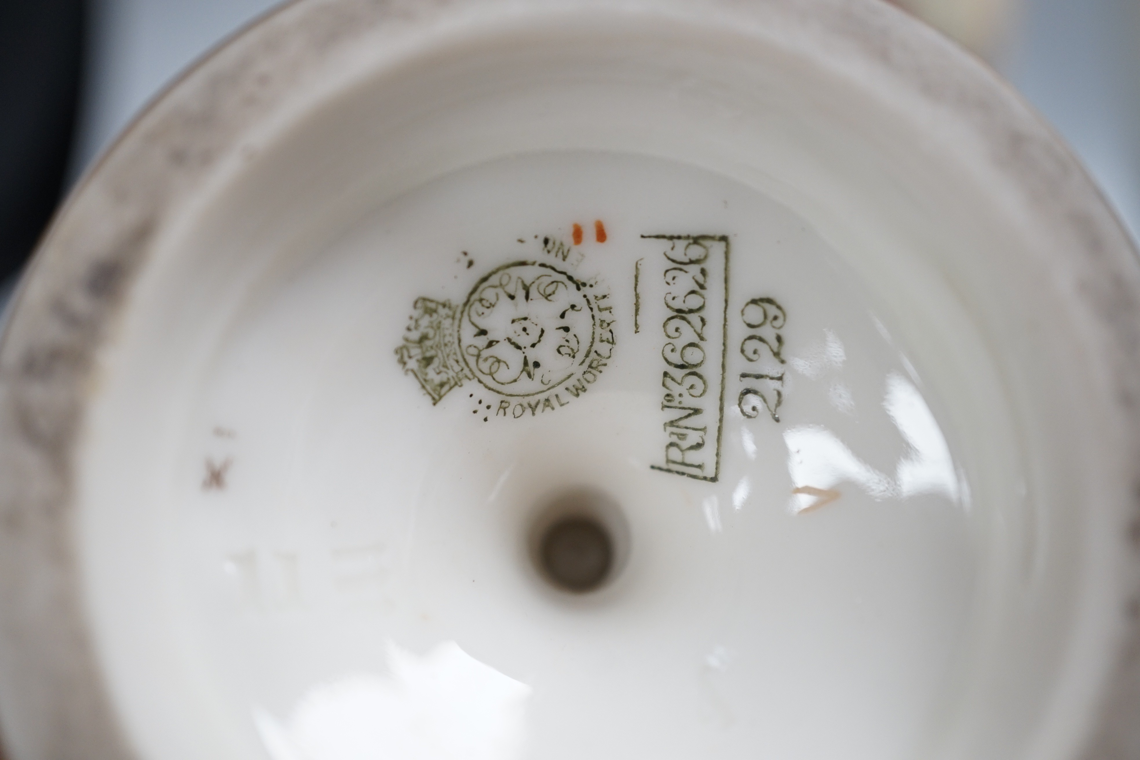 Three Royal Worcester pedestal vases, each of ovoid form and supported on circular pedestal feet, two are decorated with flowers and thistles, the other depicting a rural landscape within a gilt foliate C scroll cartouch